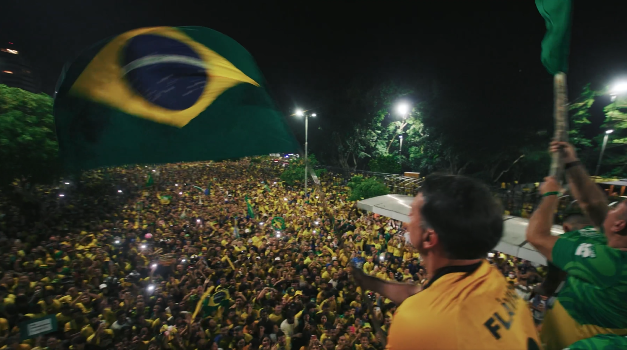 Flávio agitando a bandeira do Brasil, frente a multidão na Ponta Negra lotada.